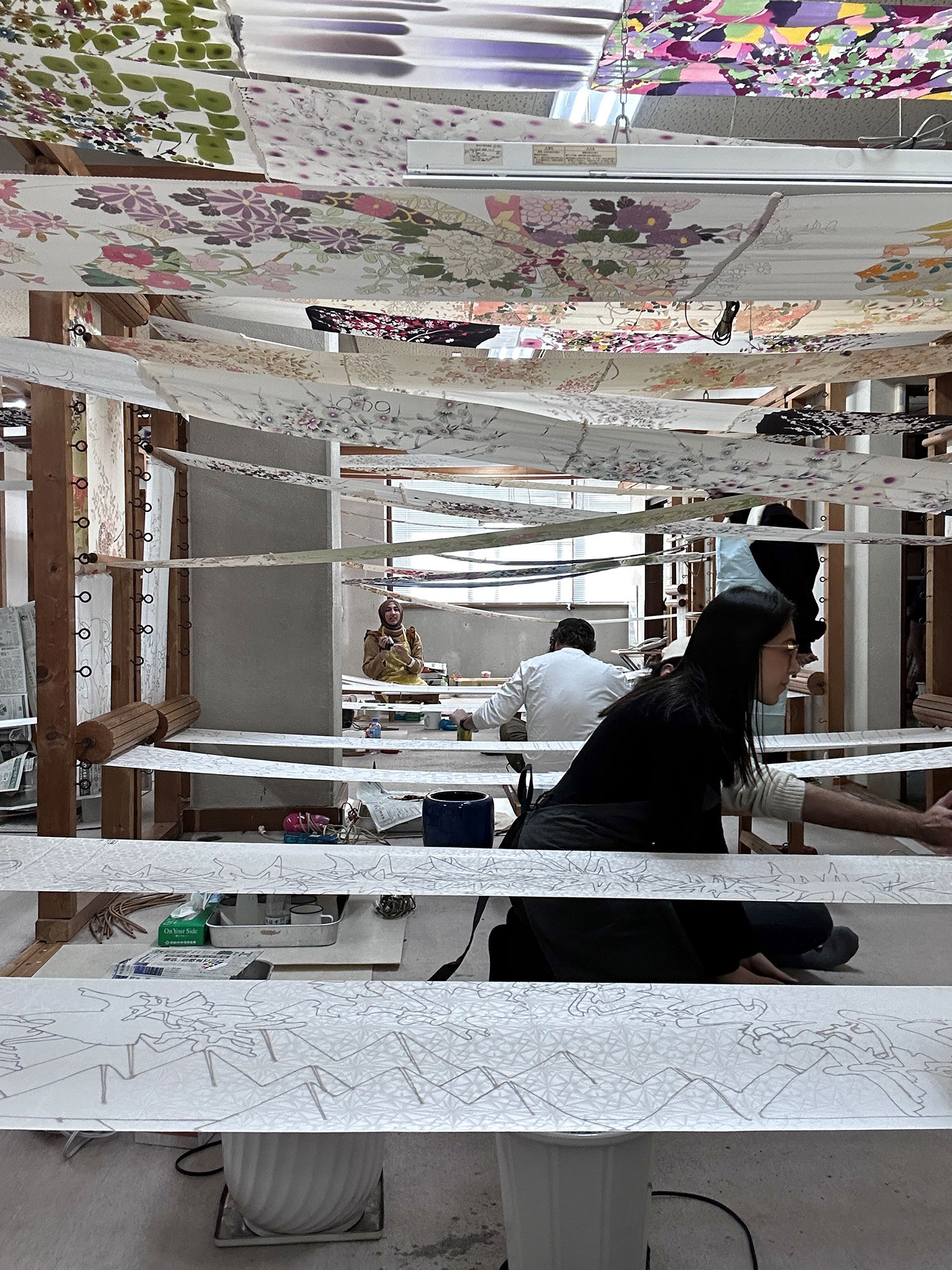 Students working between sheets of painted silk hanging above them