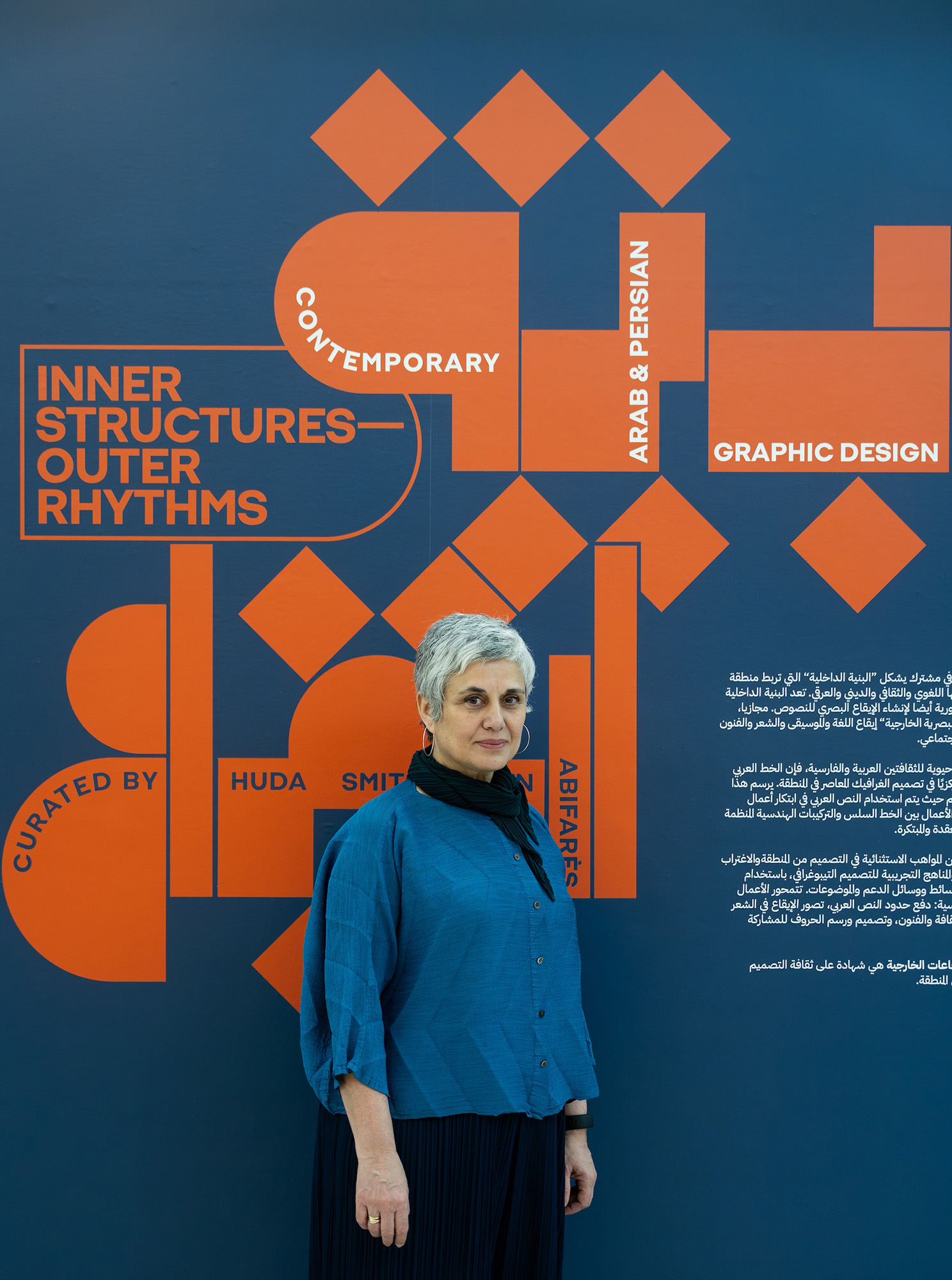 Huda standing in front of the gallery branding with the exhibition details on the wall behind her