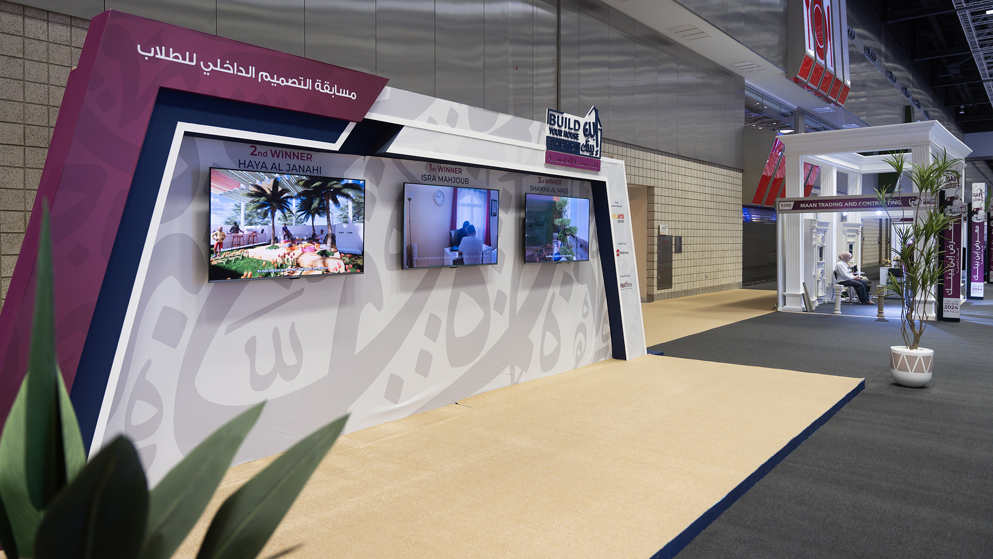a stand at build your home with three screens showing the works of the V c u arts qatar winners